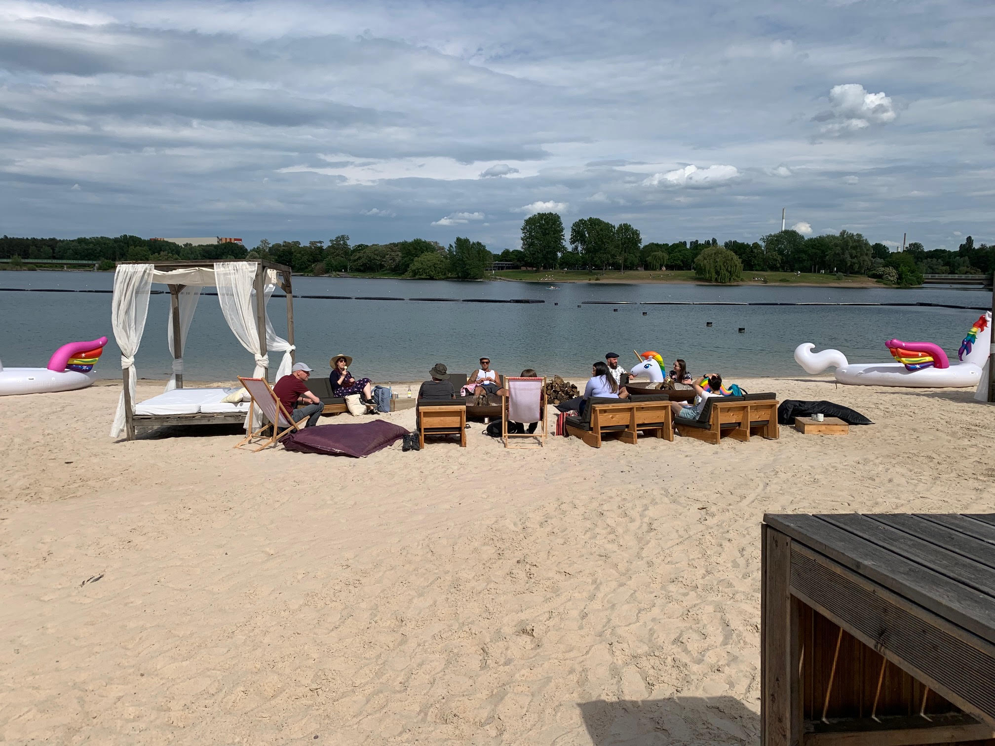 group of people sitting in the sand watching the lake